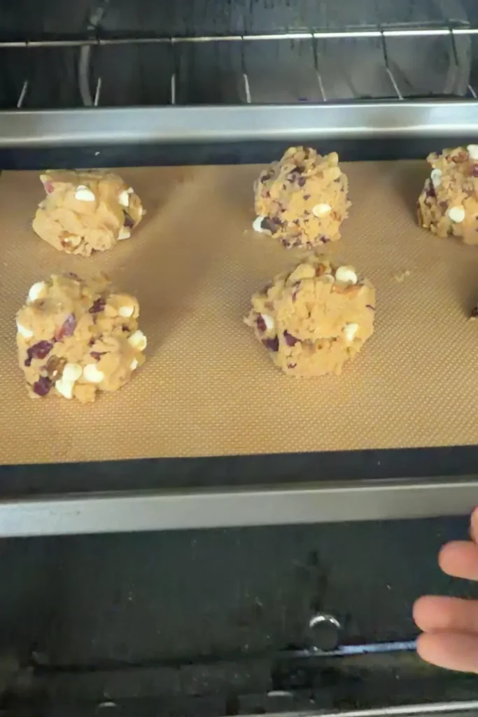 The baking tray being placed into an oven, showing the raw cookie dough balls just before baking.