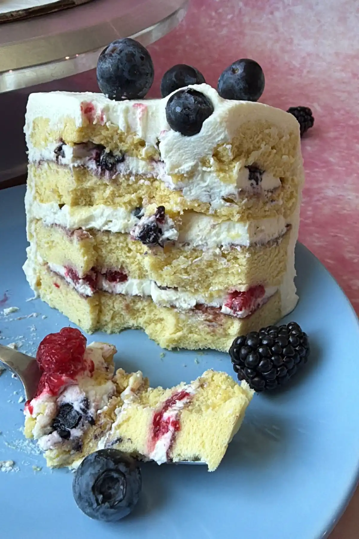 Slice of berry chantilly cake with soft chiffon sponge layers, mascarpone chantilly cream, mixed berries, and berry jam filling on a blue plate.