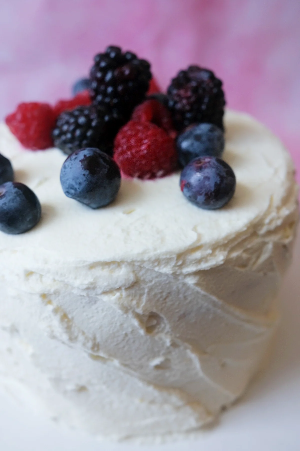 Close-up side view of berry chantilly cake frosted with light mascarpone chantilly cream and topped with mixed fresh berries.