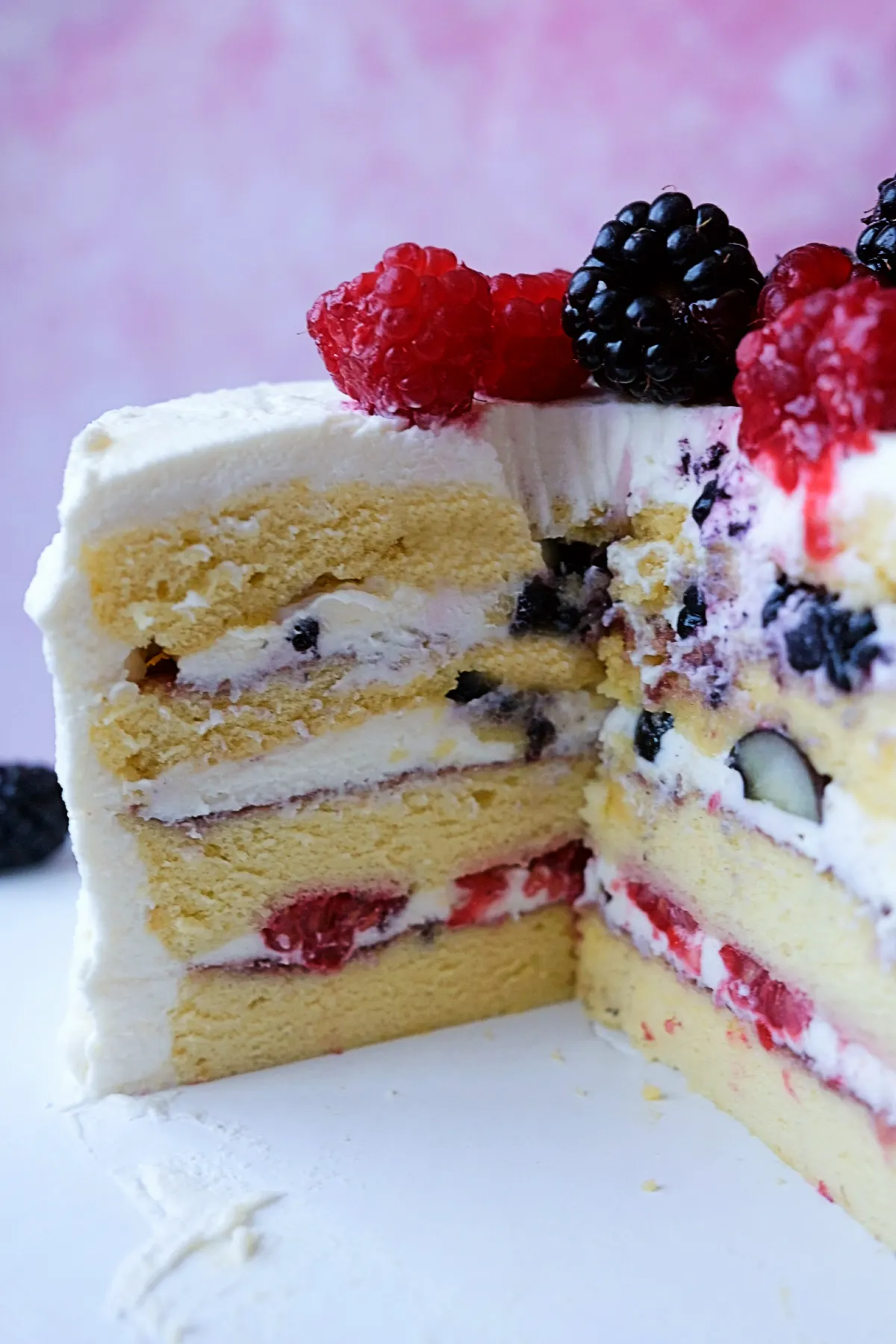 Slice removed from homemade berry chantilly cake showing fluffy chiffon sponge layers, chantilly cream, berry jam, and fresh berries.