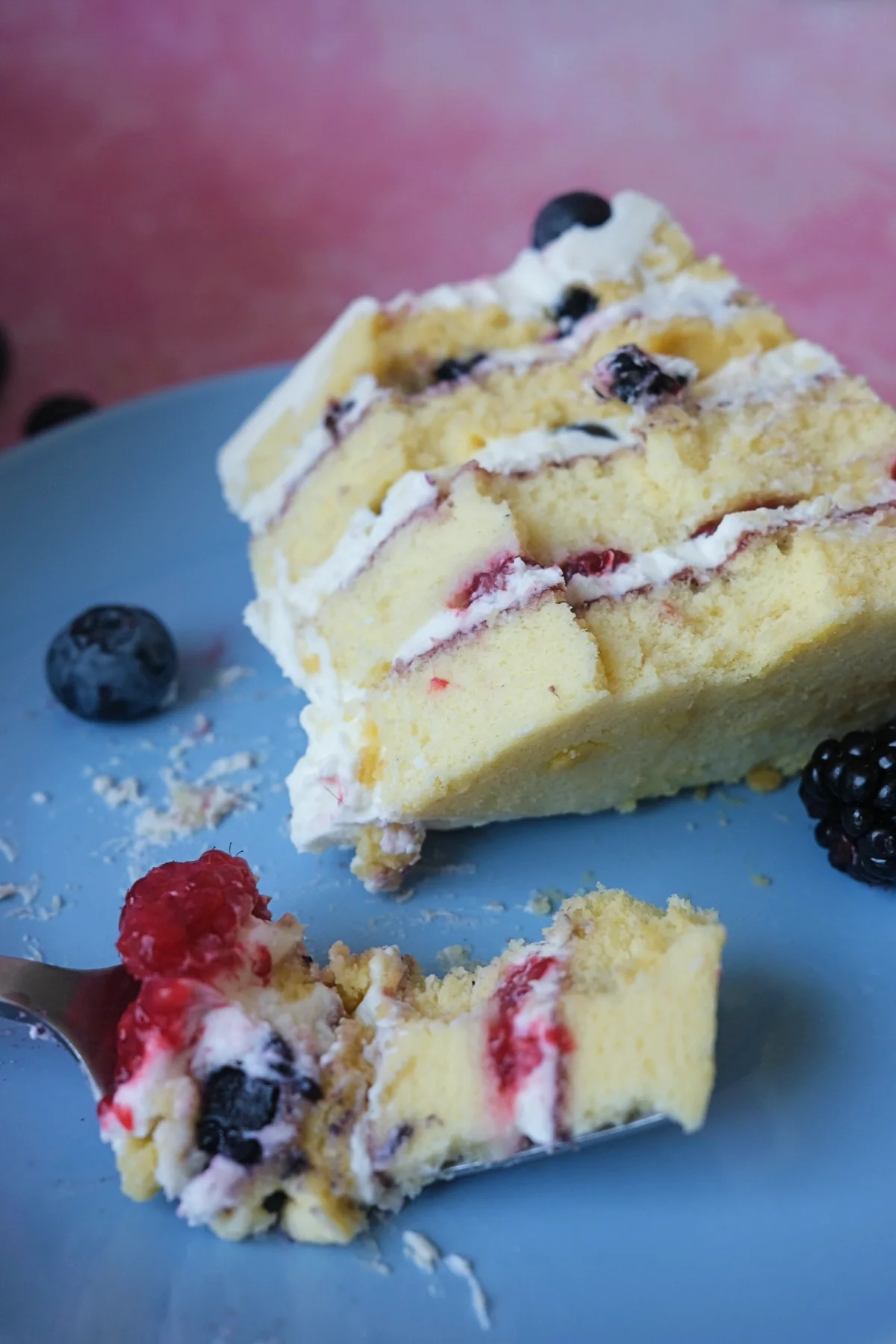 Slice of berry chantilly cake on a blue plate with layers of chiffon sponge, mascarpone chantilly cream, and mixed berries.