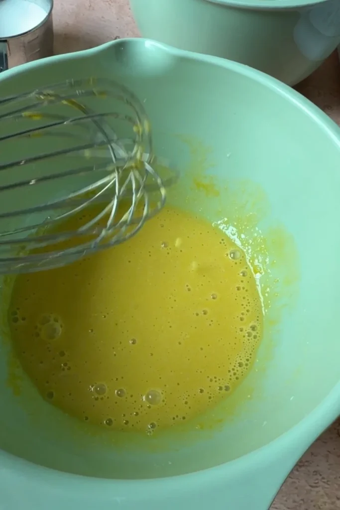 Egg yolk mixture being whisked in a mixing bowl for homemade chiffon sponge cake batter.