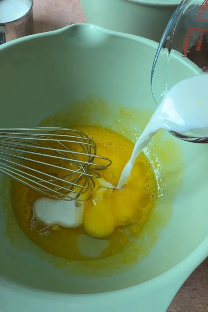 Milk being added to the egg yolk mixture while preparing chiffon cake batter.