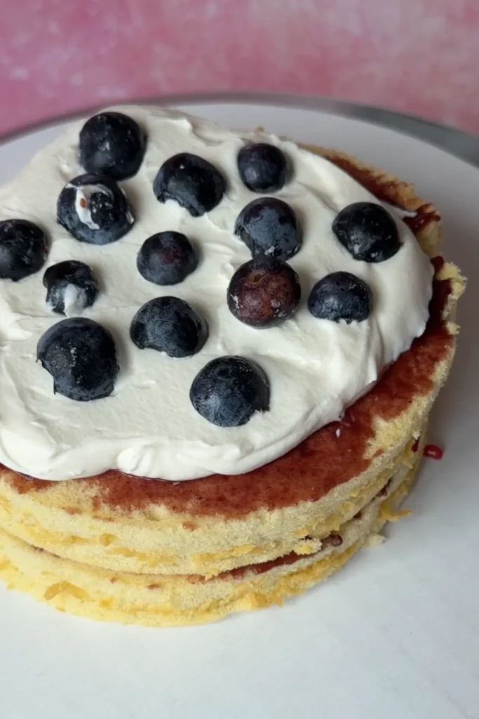 Small berry chantilly cake layered with whipped cream frosting and fresh blueberries on top.