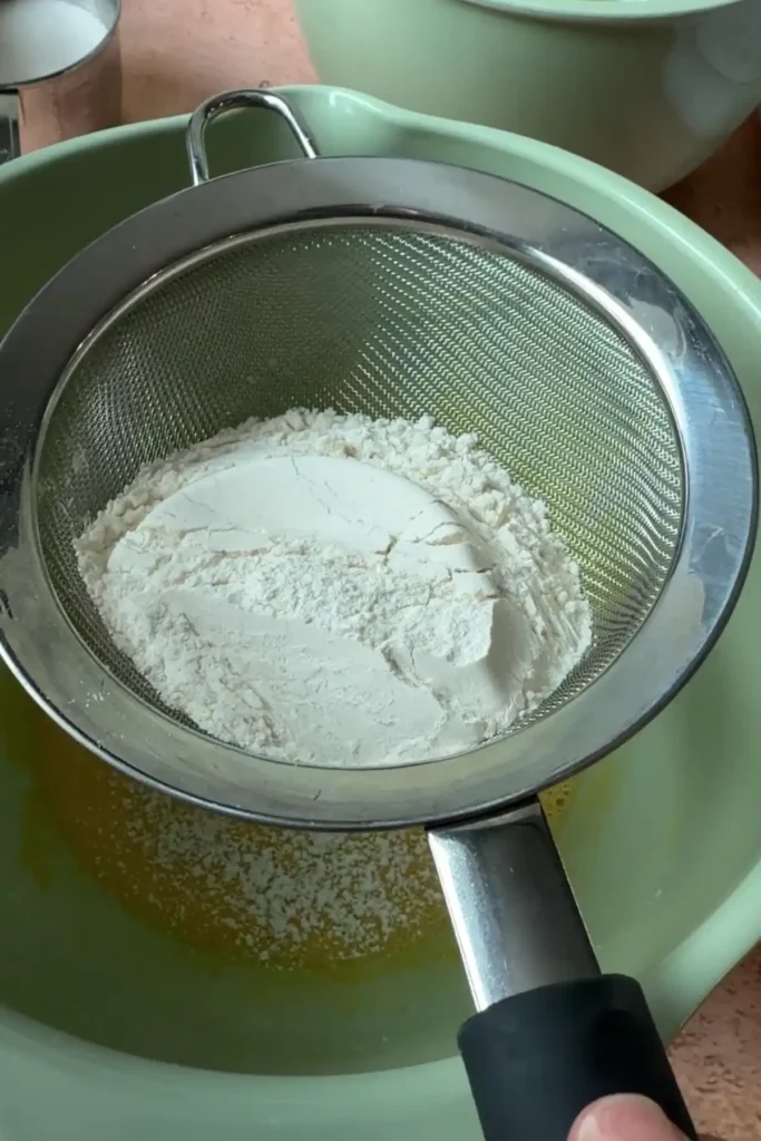 Flour and cornstarch being sifted into the egg yolk mixture for berry chantilly cake sponge layers.
