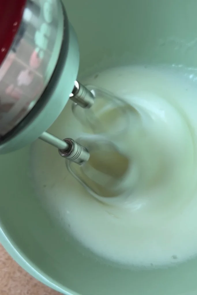 Egg whites being whipped with a hand mixer to make meringue for chiffon sponge cake.