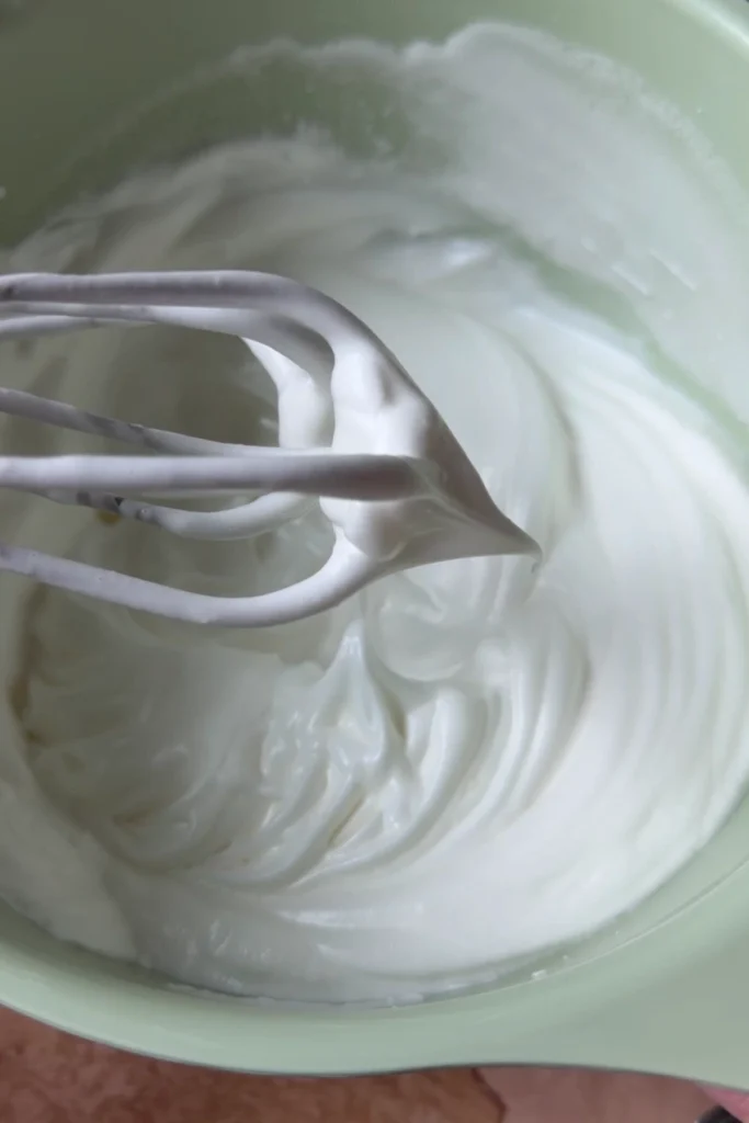 Glossy stiff egg whites with a pointed peak clinging to the whisk after whipping for chiffon sponge cake batter.