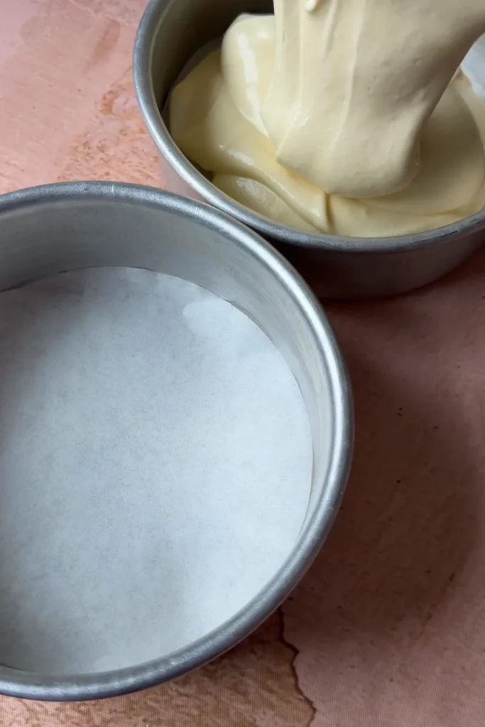 Soft chiffon cake batter being poured into small round cake pans lined with parchment paper.