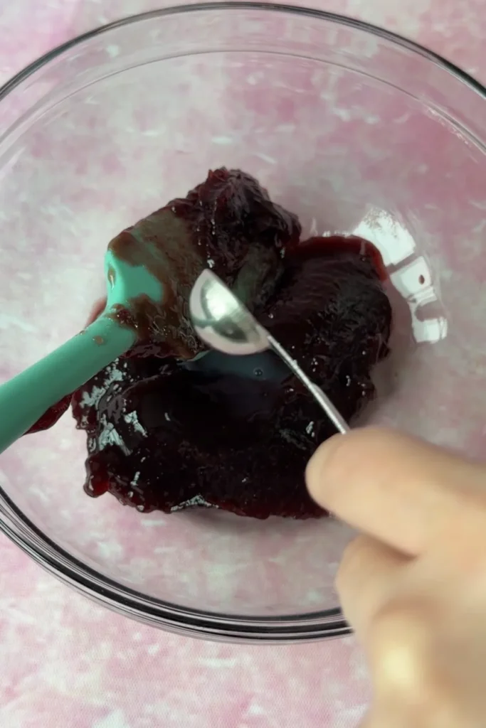 Thick berry jam in a glass bowl being loosened with liquid for spreading between cake layers.