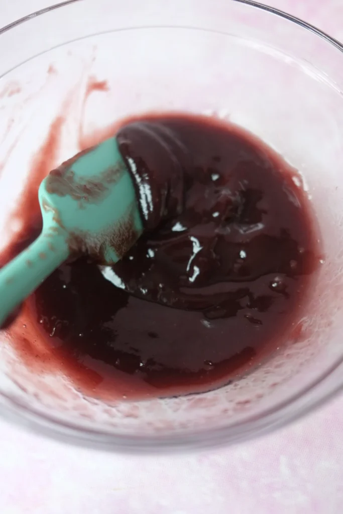 Homemade berry jam with a glossy deep purple color in a glass bowl.
