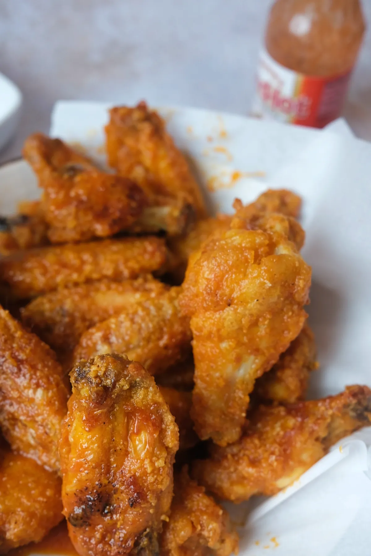 Extra crispy buffalo chicken wing held above a plate of saucy air fryer wings with hot sauce at the back.