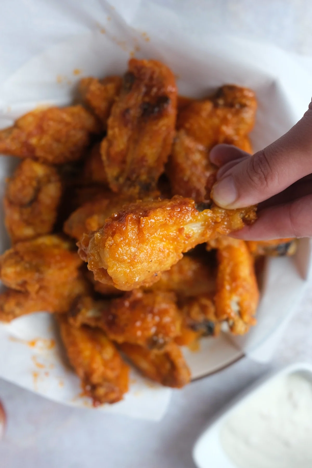 Hand holding a crispy buffalo wing coated in glossy spicy sauce over a platter of homemade air fryer wings.