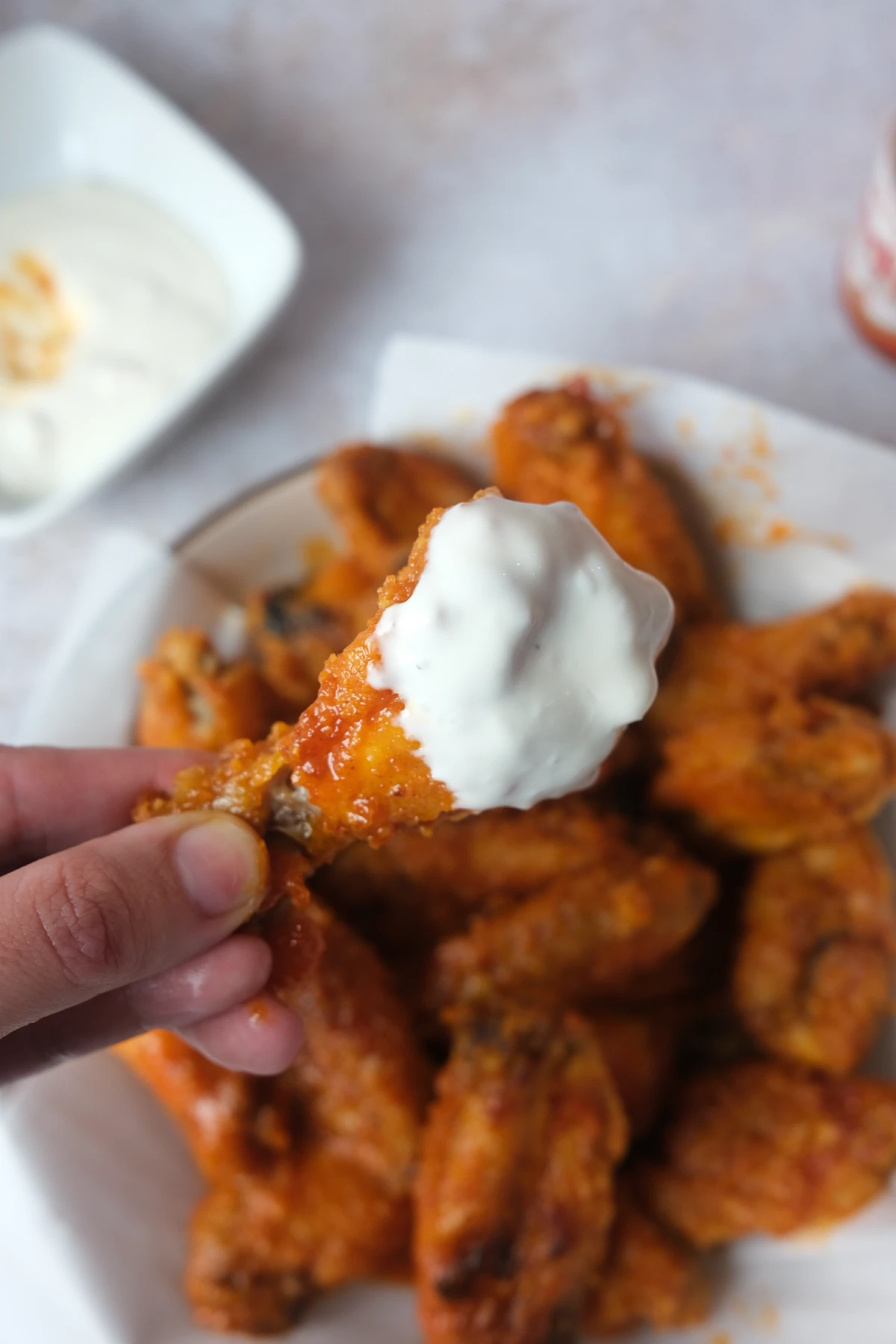 Close-up of a crispy buffalo chicken wing dipped in creamy ranch dressing with a platter of air fryer buffalo wings blurred in the background.