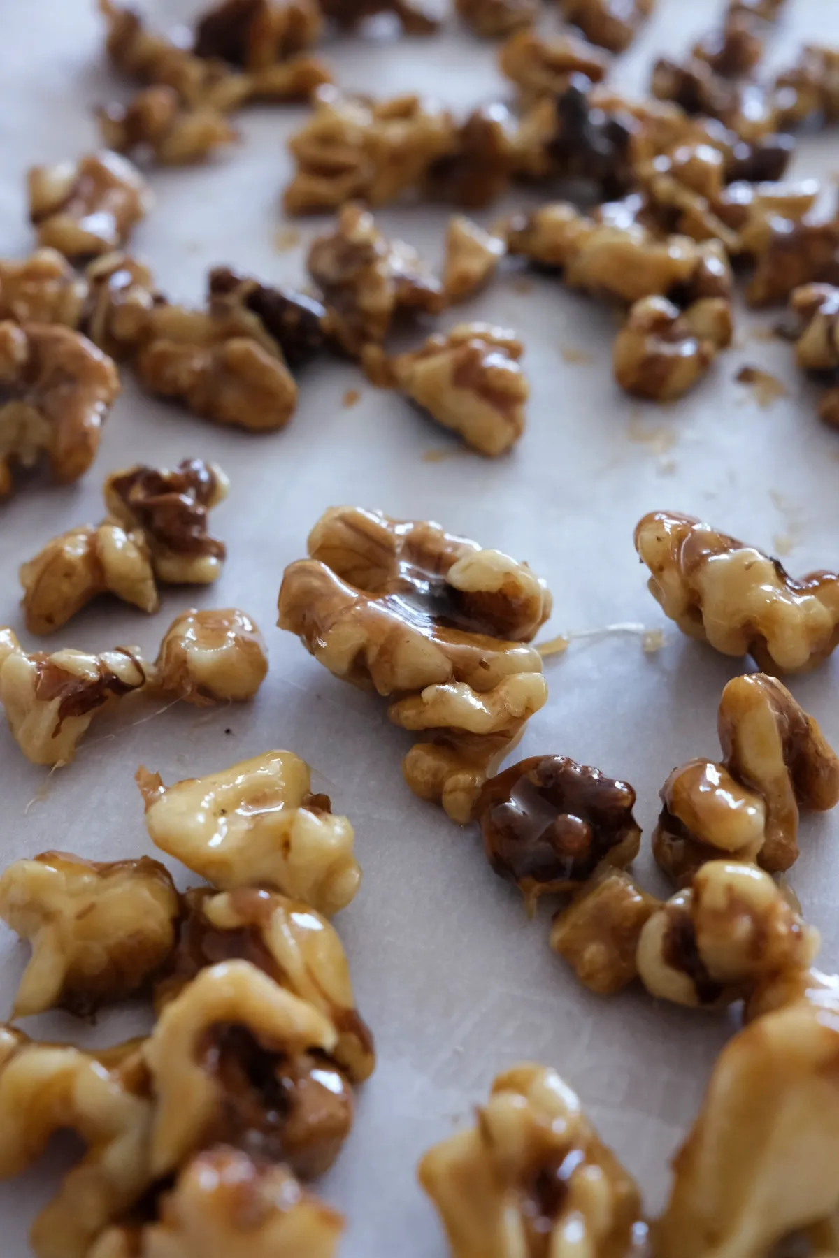 Sweet candied walnuts with a shiny caramelized coating spread out on parchment paper.