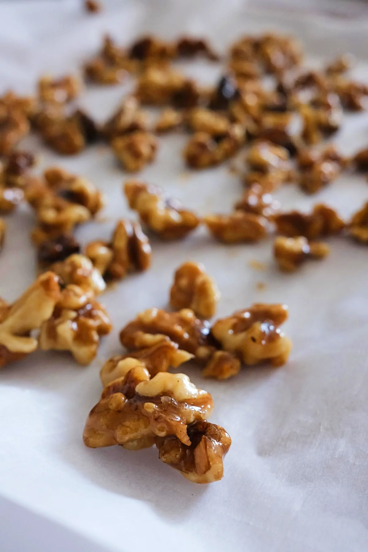 Candied walnuts with a crisp sugary coating scattered across a parchment-lined tray.