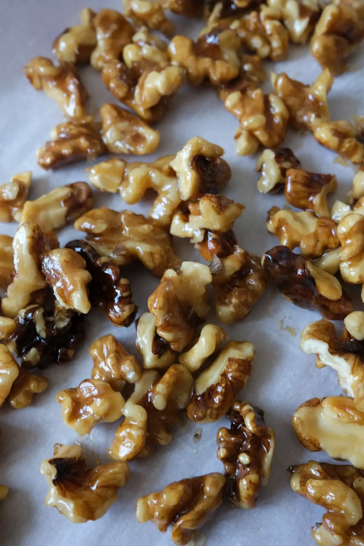 Close-up of glossy homemade candied walnuts cooling on parchment paper.