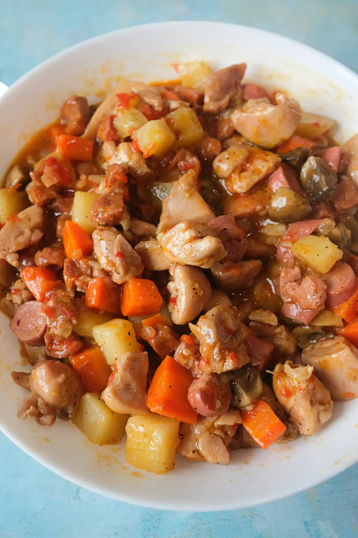 Chicken pastel in a white bowl with chicken, carrots, potatoes, mushrooms, chorizo, and Vienna sausages in a savory sauce.