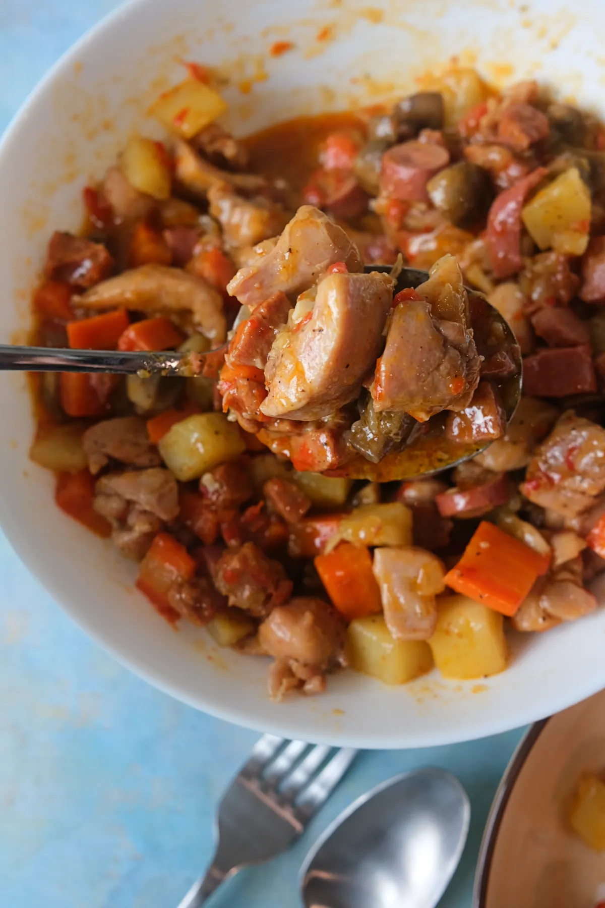 Spoonful of chicken pastel lifted from a bowl, showing tender chicken, mushrooms, potatoes, carrots, and sausage.