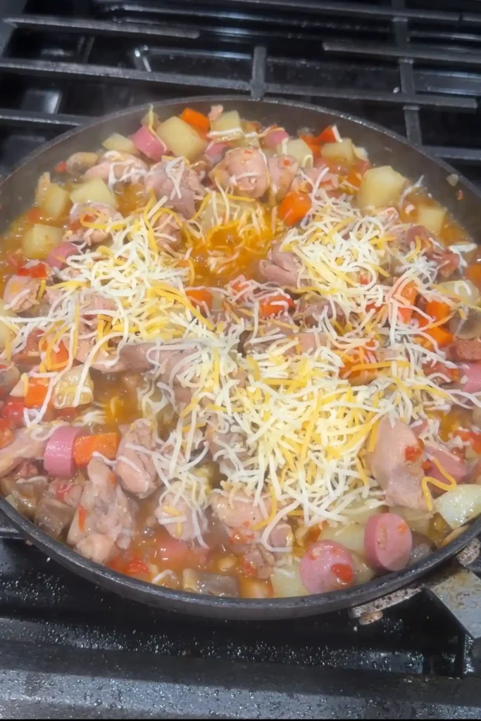 Shredded cheese sprinkled over simmering chicken pastel with vegetables, sausage, and chicken.
