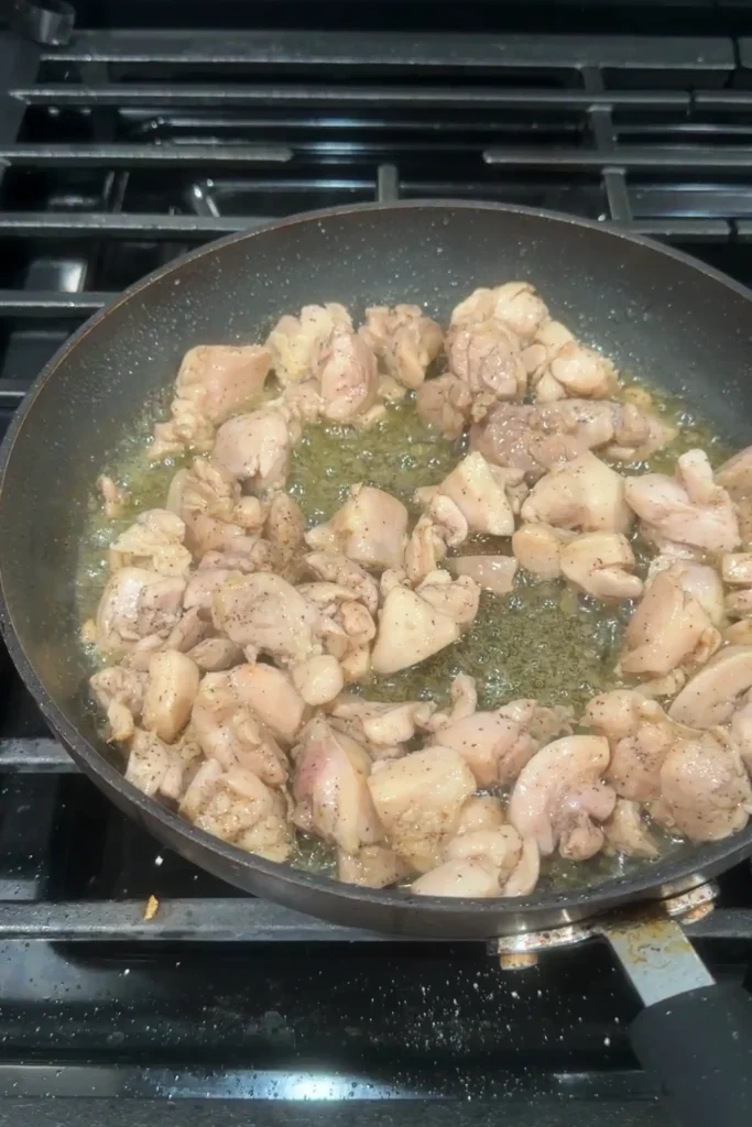 Seasoned chicken pieces lightly browned and sizzling in a skillet with rendered juices and oil.
