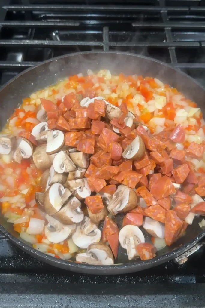 Chorizo, Vienna sausage, mushrooms, onions, and bell peppers added to the skillet with sautéed vegetables.