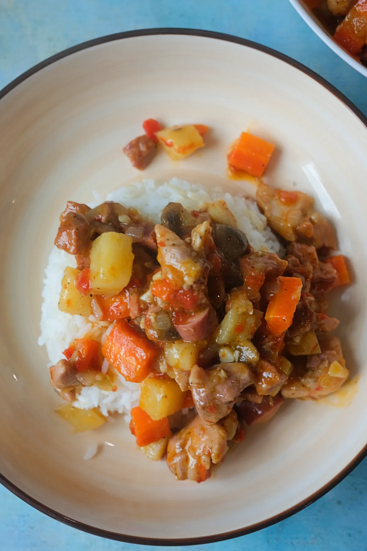 Chicken pastel spooned over steamed rice in a shallow bowl, with potatoes, carrots, mushrooms, and sausage throughout.