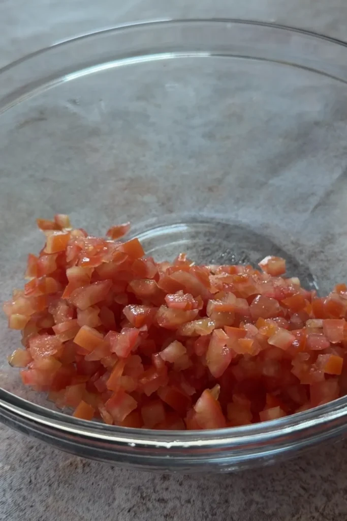 Finely diced tomatoes in a clear glass bowl for homemade chunky salsa.