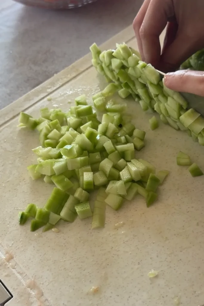 Chopping peeled cucumber into small cubes on a cutting board for fresh salsa.