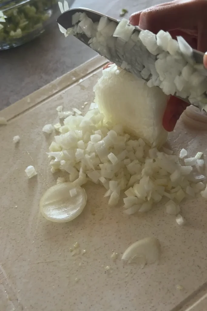 Finely dicing white onion on a cutting board for homemade salsa recipe.