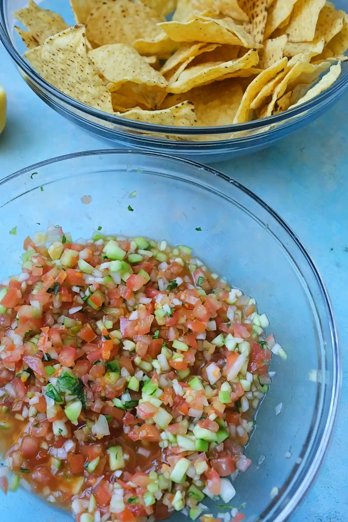 Fresh chunky salsa in a glass bowl with tortilla chips in the background.