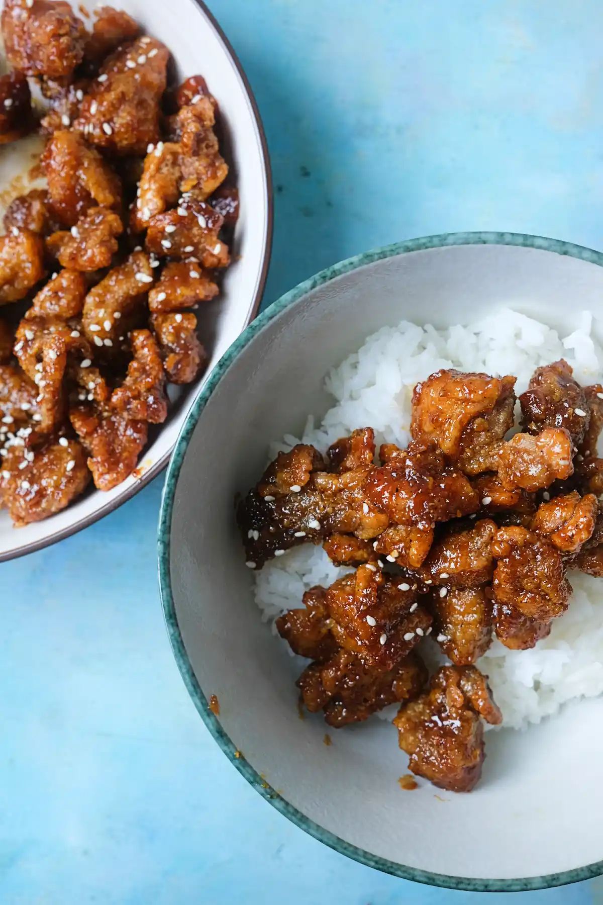 Crispy honey garlic chicken served over white rice with sesame seeds and extra chicken on the side.