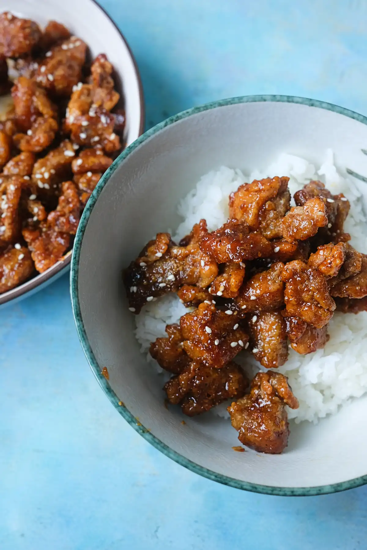 Crispy honey garlic chicken served over white rice with sesame seeds and extra chicken on the side.