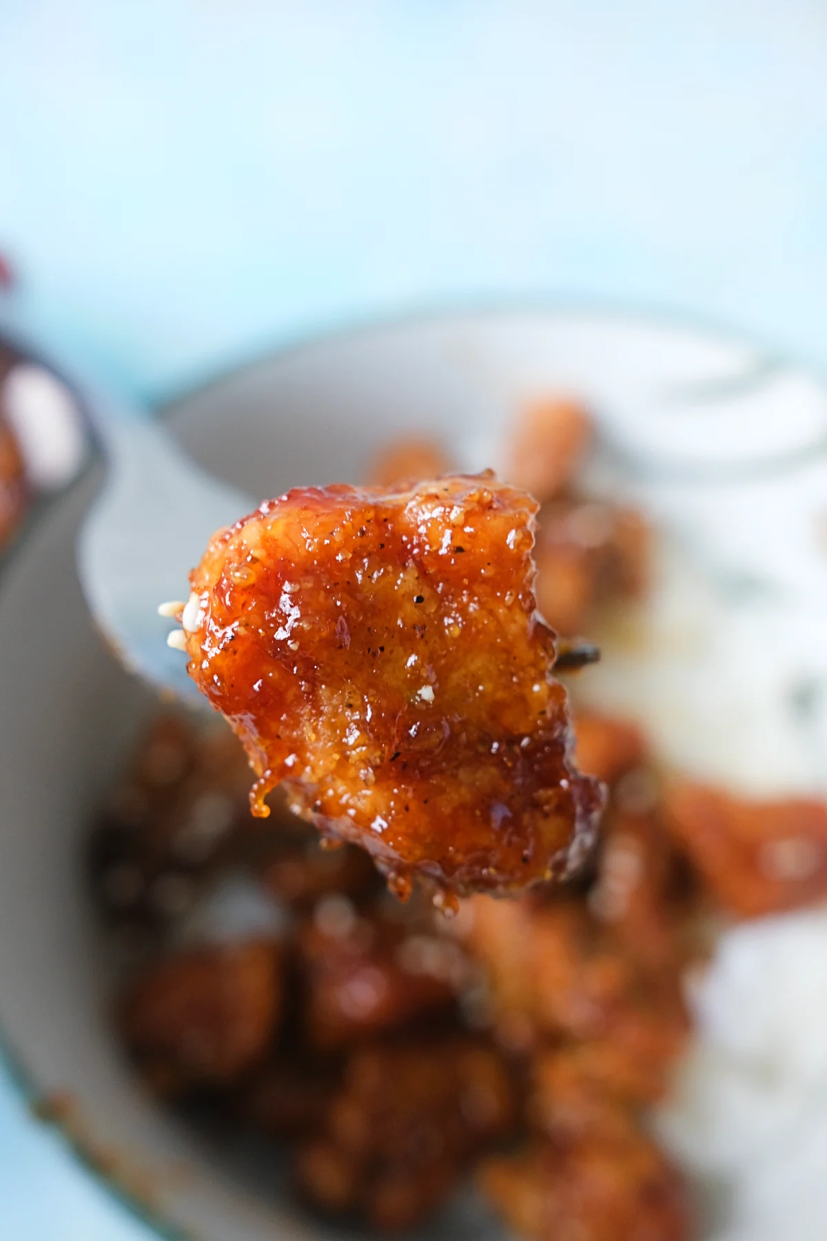 Close-up of a crispy honey garlic chicken piece coated in sticky sauce on a fork.