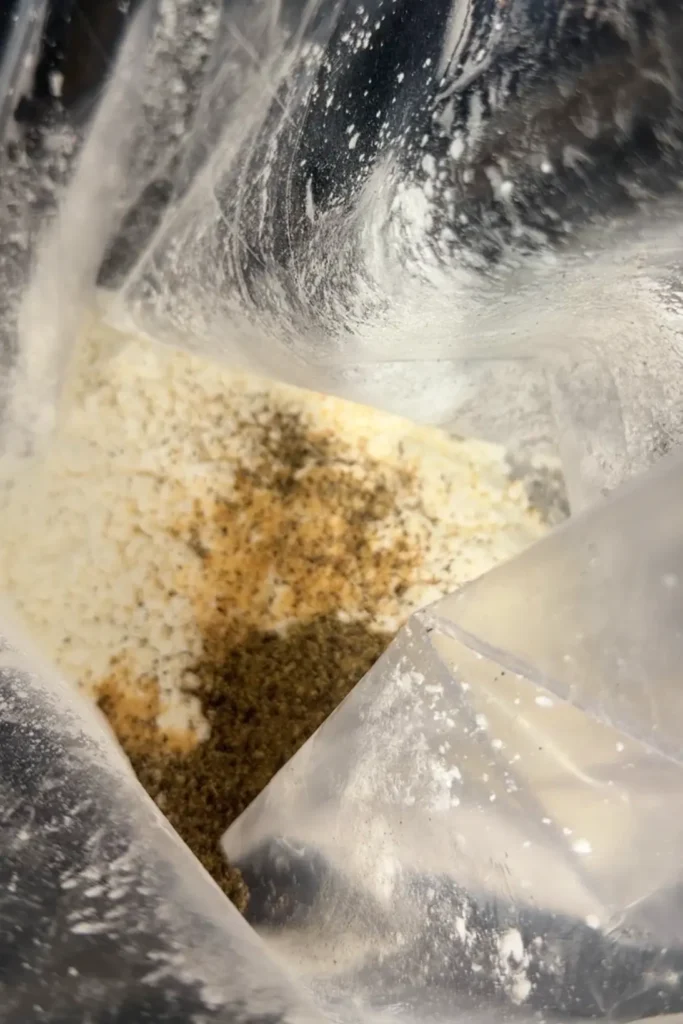 Seasoned cornstarch mixture with garlic powder, salt, and black pepper inside a zip-top bag for coating chicken.