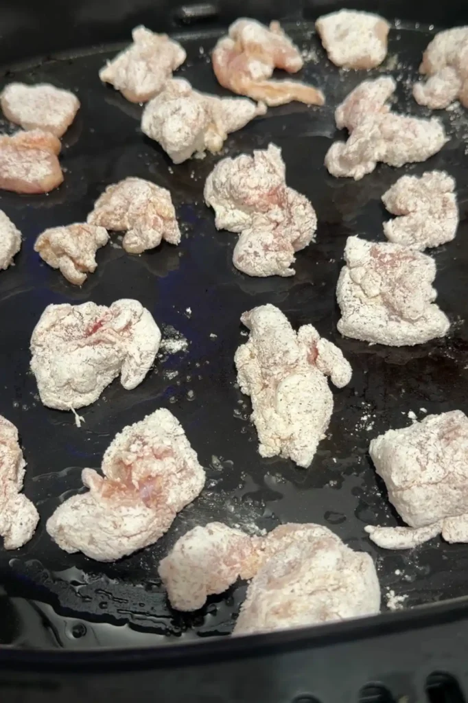 Bite-sized chicken pieces coated in seasoned cornstarch arranged in an air fryer basket.