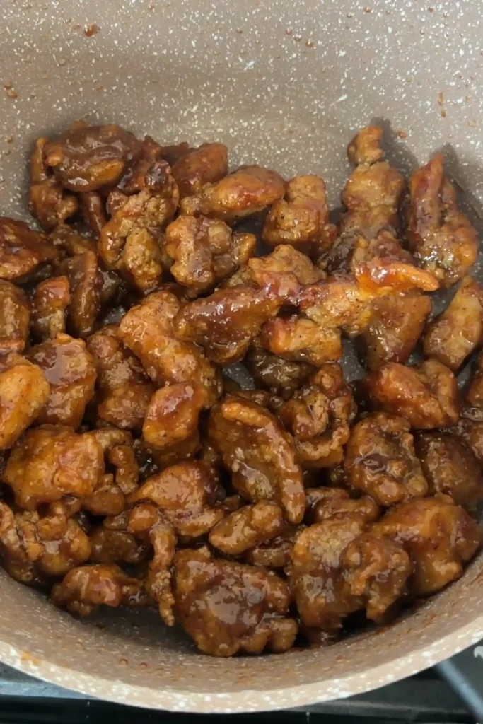 Crispy chicken tossed in glossy honey garlic sauce in a saucepan.
