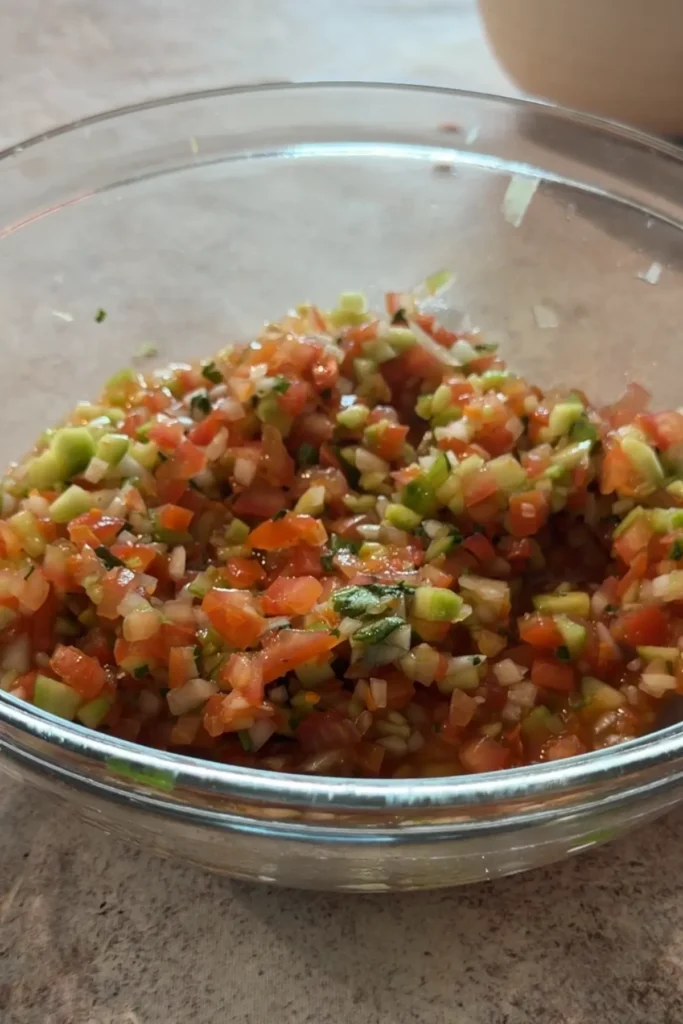 Fresh chunky salsa mixed together in a glass bowl with visible diced vegetables.