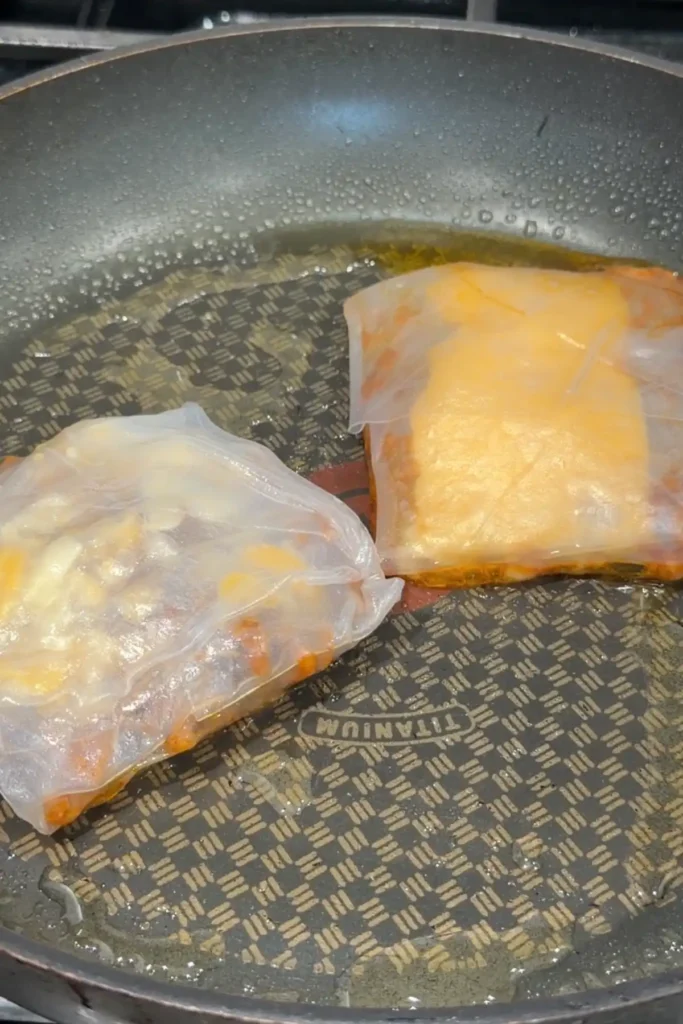 Folded rice paper dumplings frying in a pan with a thin layer of oil.