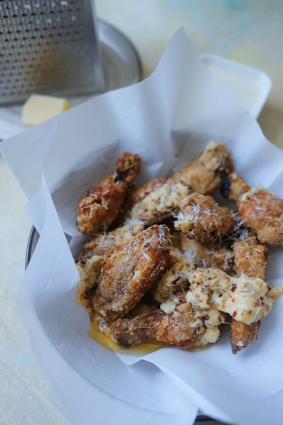 Golden garlic parmesan chicken wings in a paper-lined basket with freshly grated parmesan on top.