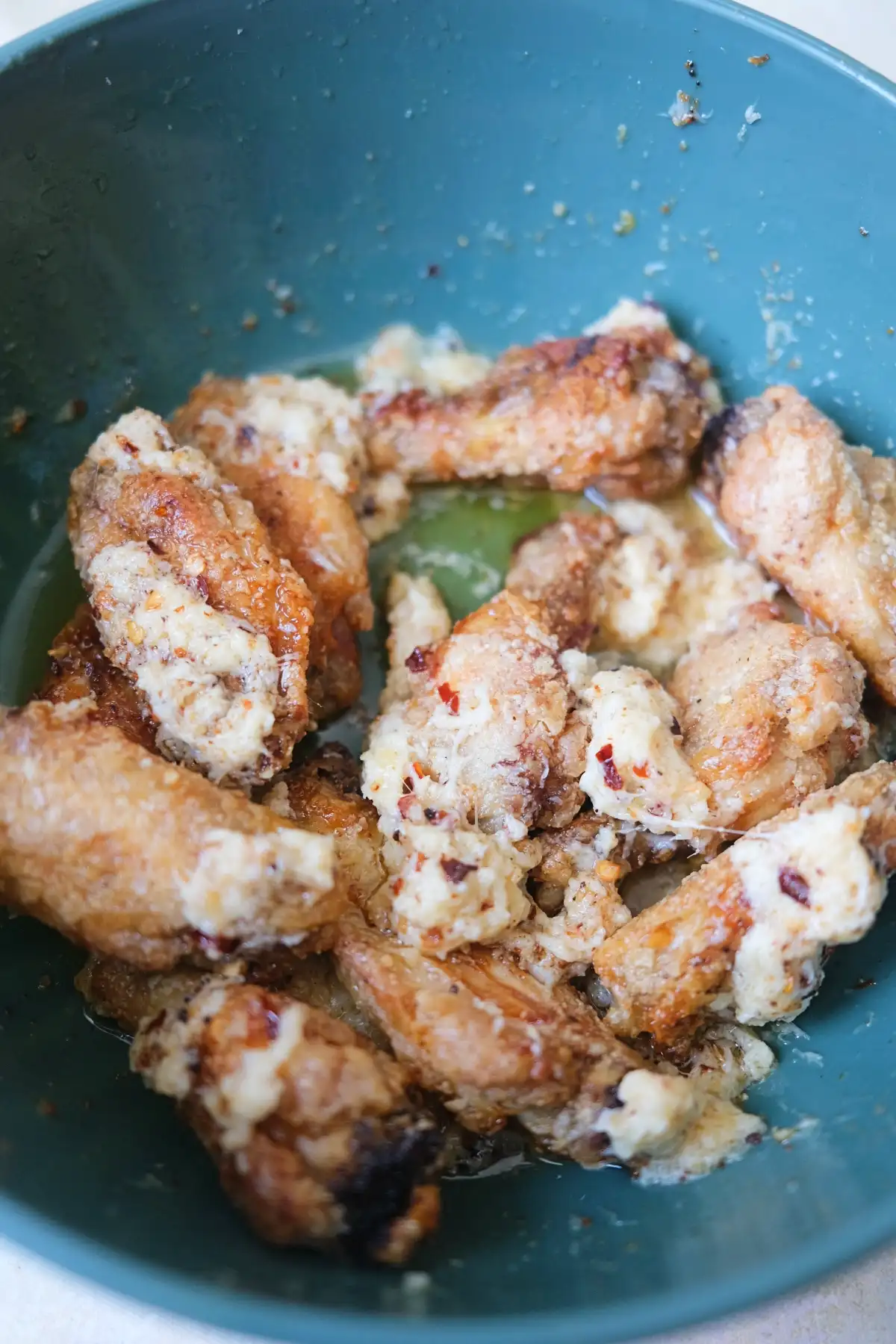 Close-up of crispy air fryer chicken wings coated in creamy garlic parmesan sauce inside a green bowl.