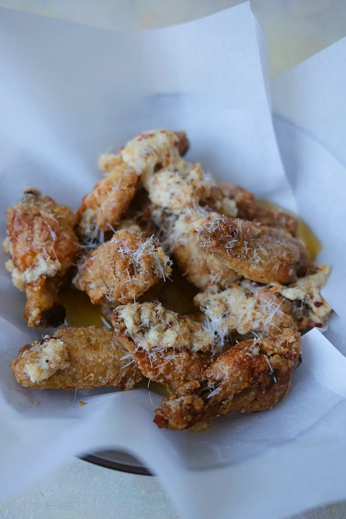 Air fryer garlic parmesan wings piled in a parchment-lined bowl with extra parmesan cheese sprinkled on top.