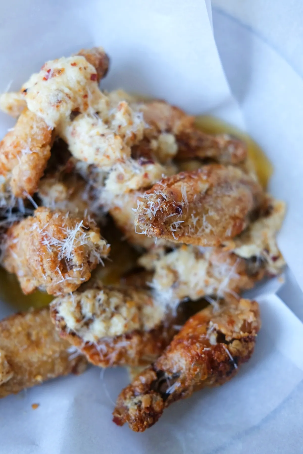 Close-up of crispy golden chicken wings coated in creamy garlic parmesan sauce with grated parmesan garnish.