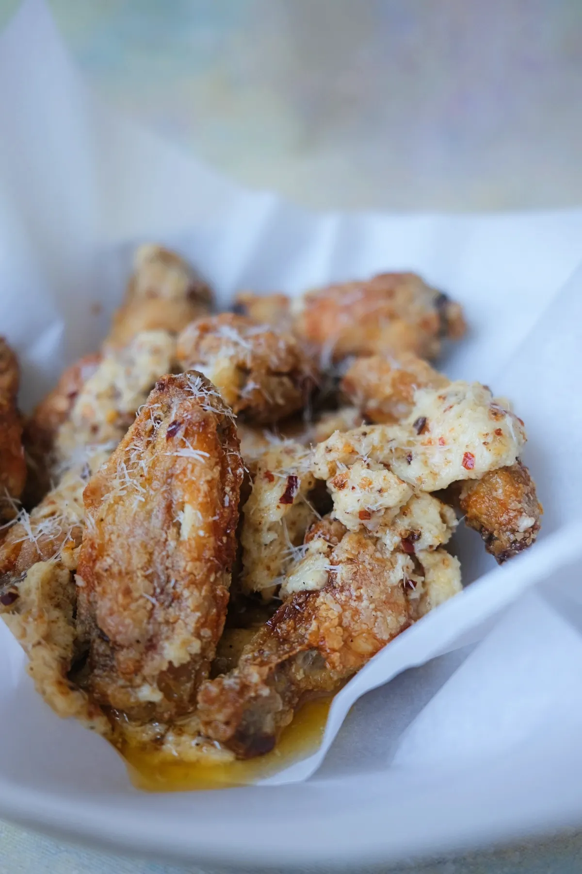 Crispy garlic parmesan wings in a parchment-lined serving bowl with buttery parmesan sauce underneath.