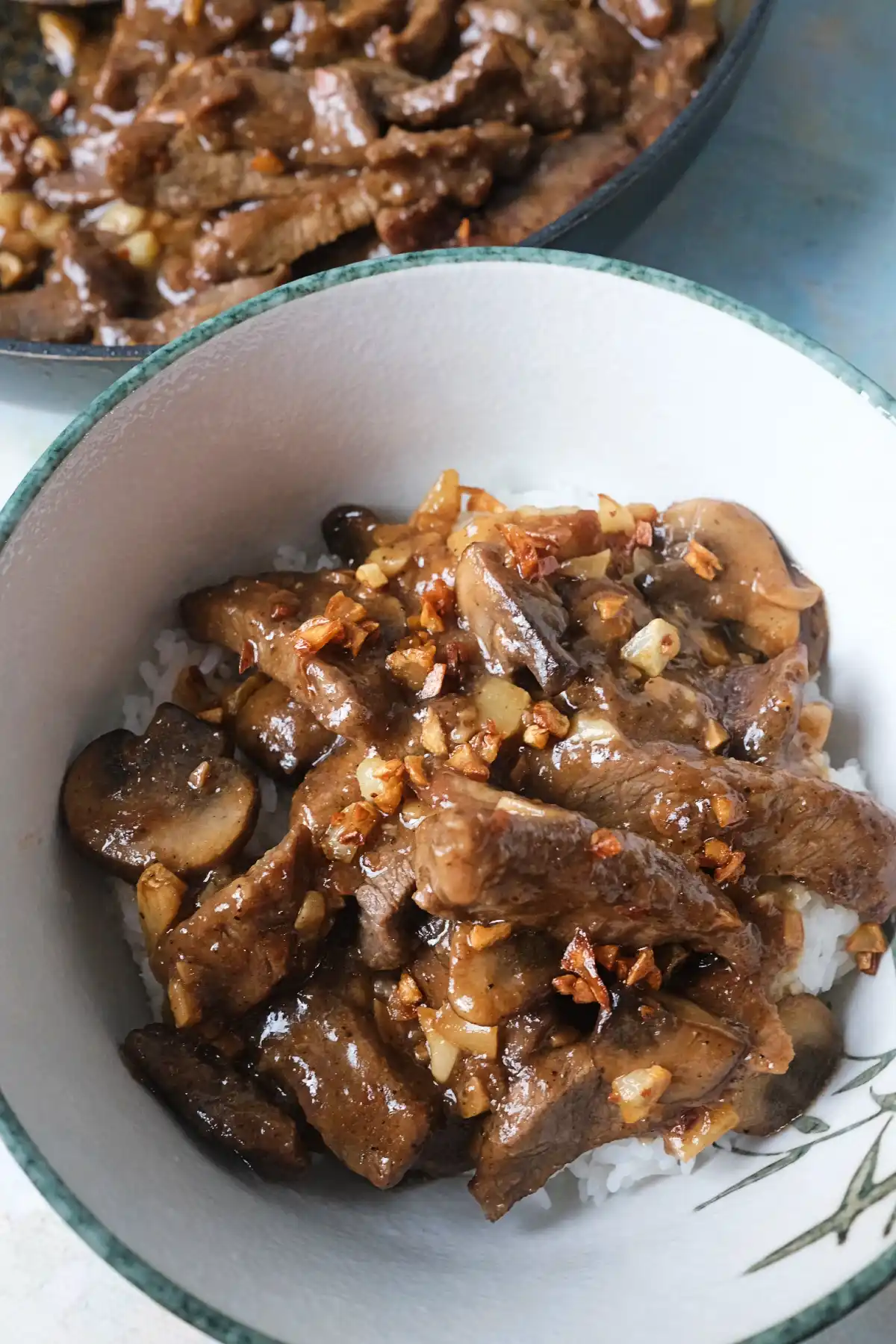 Bowl of mushroom pepper steak over white rice topped with crispy garlic and glossy garlic pepper sauce.