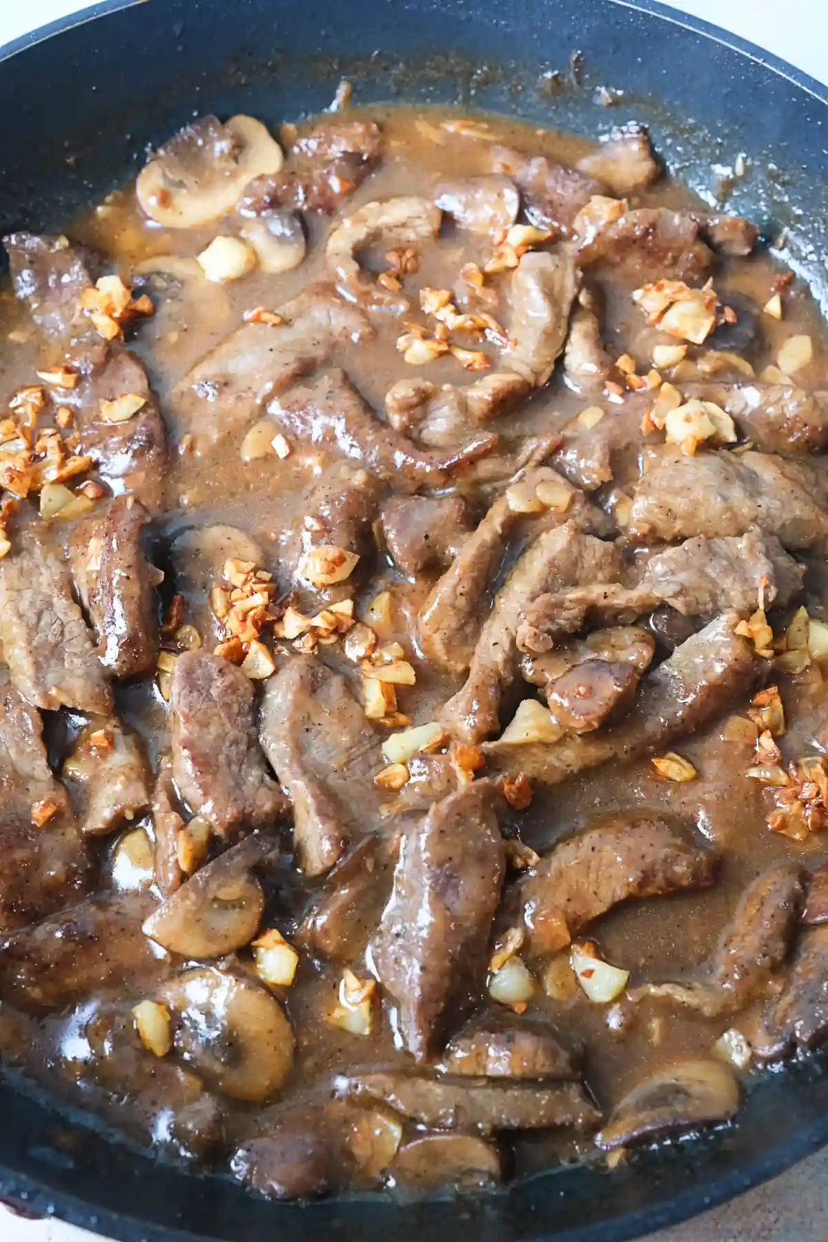 Mushroom pepper steak simmering in a skillet with rich savory sauce and crispy garlic.