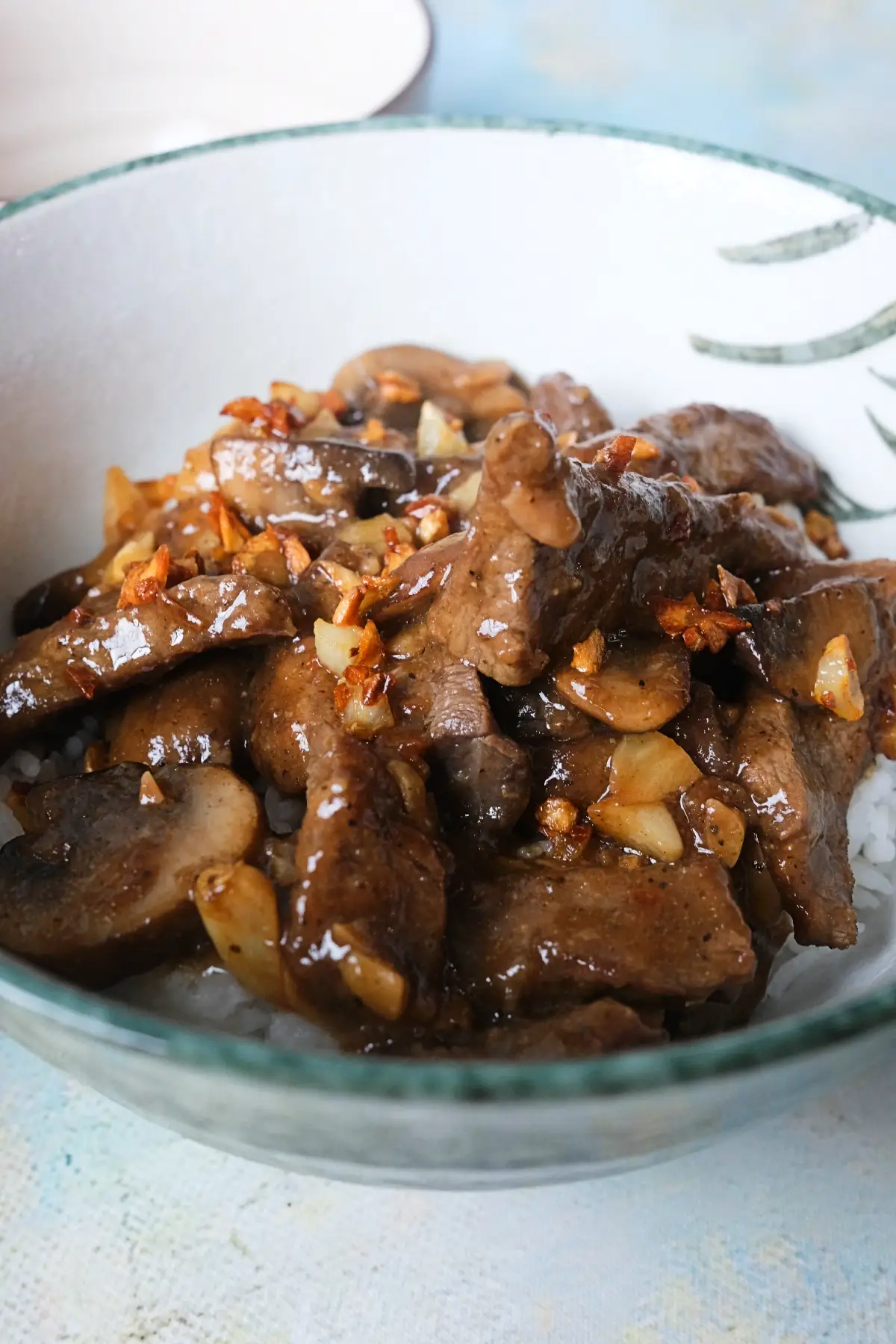 Tender slices of garlic pepper beef and mushrooms served over rice in a ceramic bowl.