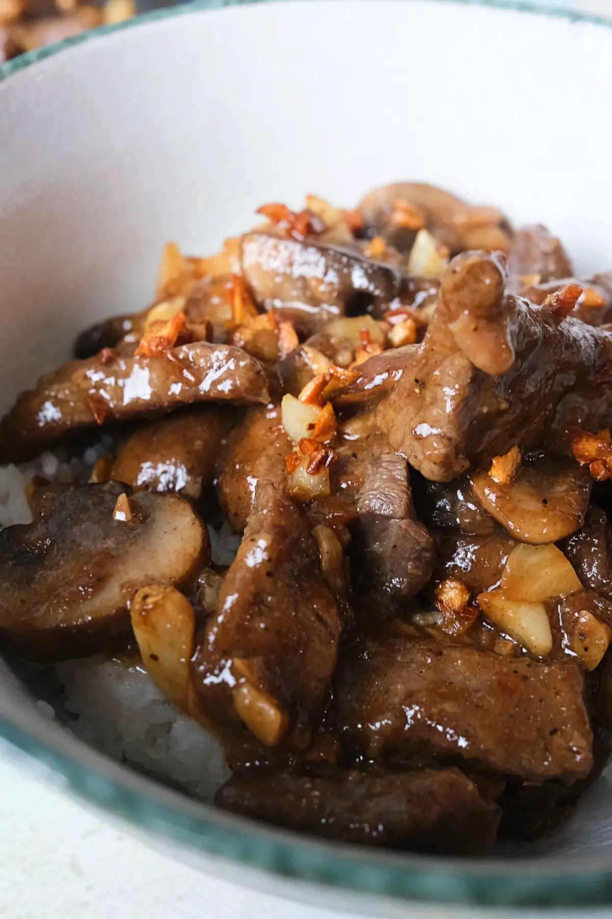 Close-up of glossy mushroom pepper steak with caramelized mushrooms and crispy garlic topping.
