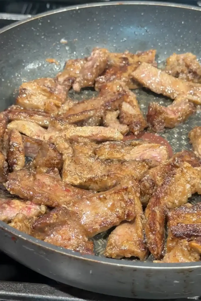 Garlic pepper beef searing in a pan with caramelized edges and browned surfaces.