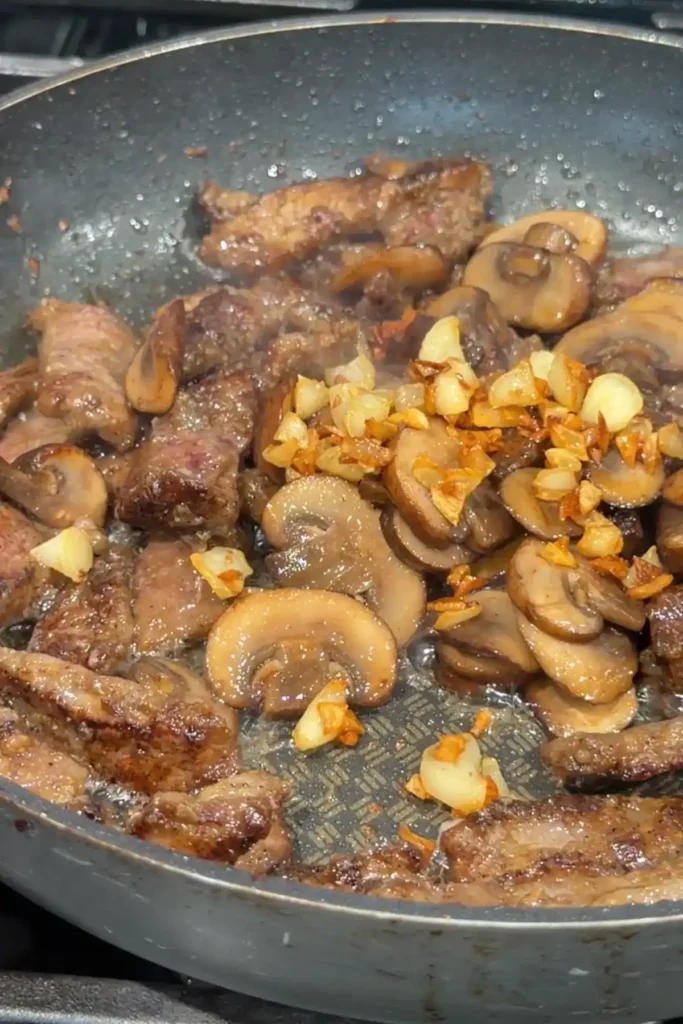 Cooked beef and sautéed mushrooms topped with crispy fried garlic in a skillet.