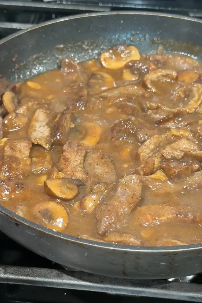 Garlic pepper beef simmering in a rich brown gravy with mushrooms.